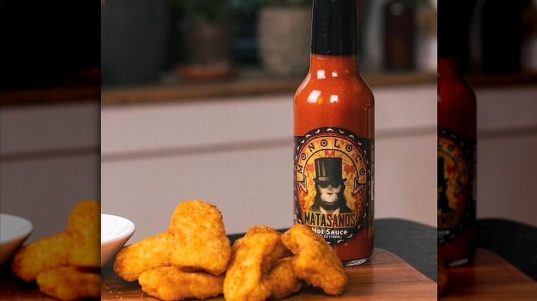 A bottle of Chile Monoloco Matasanos Hot Sauce next to chicken nuggets.