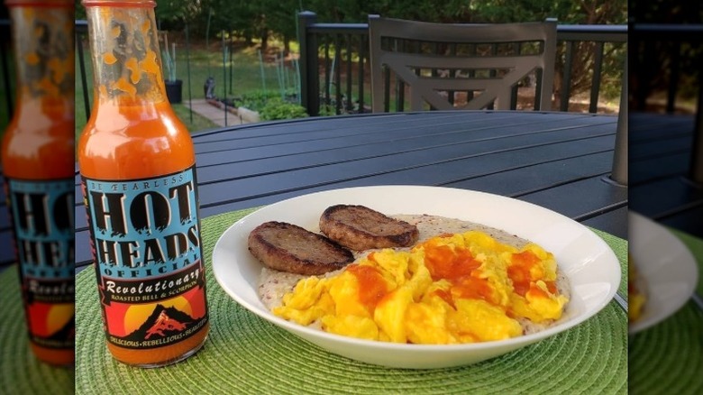 A bottle of Hot Heads Official Revolutionary Hot Sauce next to grits and sausage.
