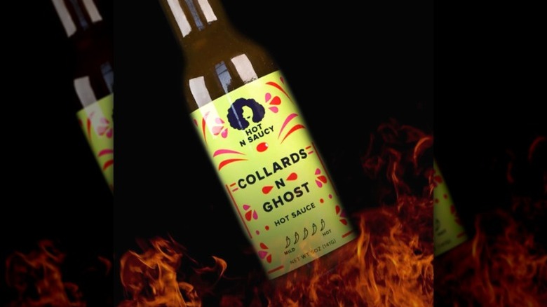 A bottle of Hot N Saucy Collards N Ghost Hot Sauce in front of flames.
