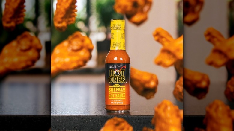 A bottle of Hot Ones Original Buffalo Hot Sauce with falling chicken wings.