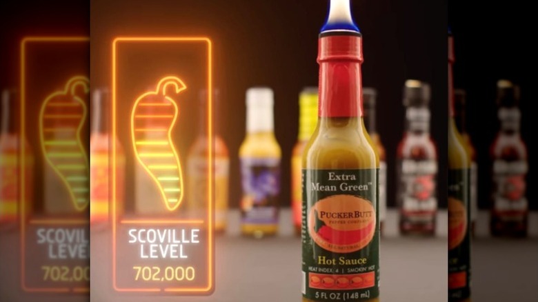 A bottle of Extra Mean Green Hot Sauce on fire, next to the "Hot Ones" Scoville scale.