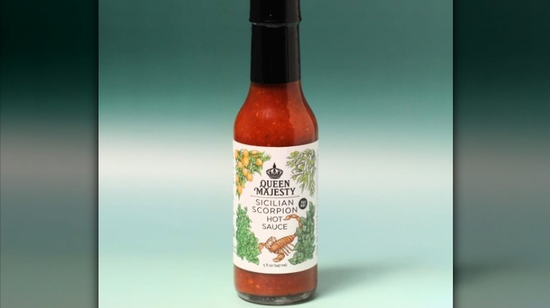 A bottle of Queen Majesty Sicilian Scorpion Hot Sauce against a blue-green gradient background.