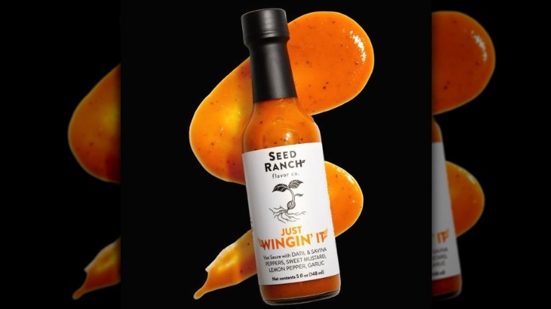 A bottle of Seed Ranch Flavor Co Just Wingin' It Hot Sauce in front of an artful smear of sauce.