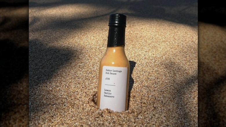 A bottle of Senor Lechuga 0.006 Hot Sauce in the sand.