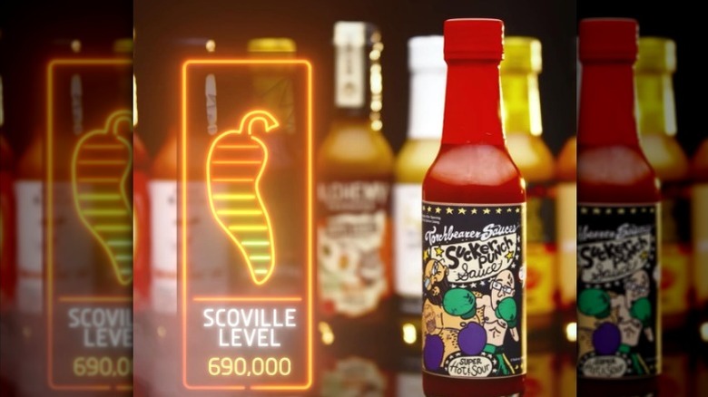 A bottle of Torchbearer Sauces Sucker Punch Super Hot Sauce next to the "Hot Ones" Scoville scale.