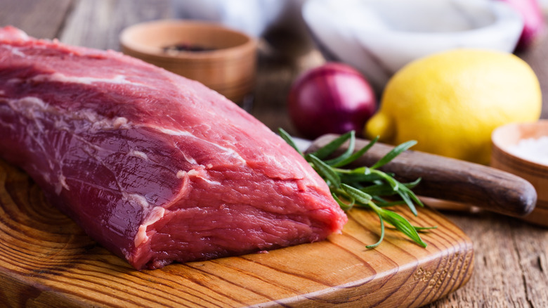 Raw beef tenderloin on a wooden board with lemon, herbs, and onion