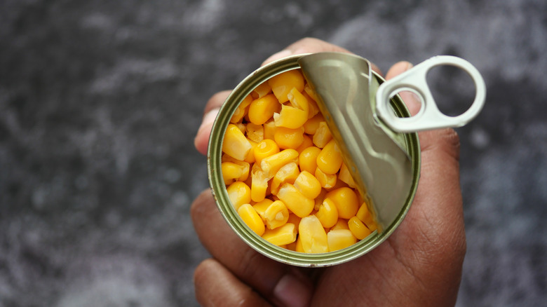 Top view of hand holding an open can of corn
