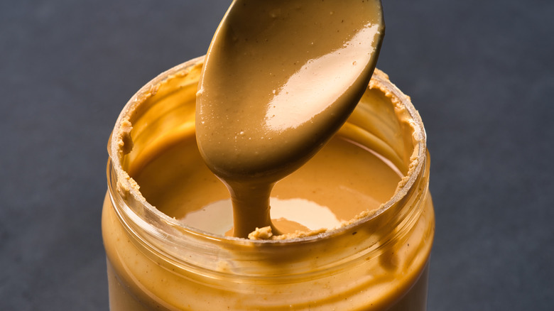 A container of peanut butter with a spoon drizzling peanut butter into it