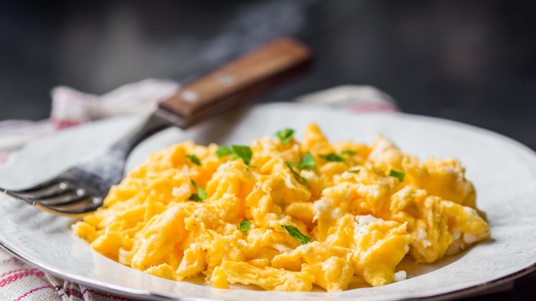 Scrambled eggs topped with fresh herbs on plate with fork