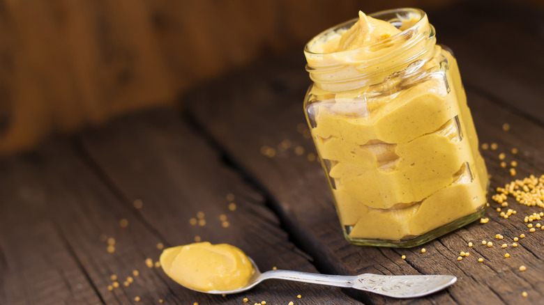 Clear jar of homemade mustard next to teaspoon of mustard