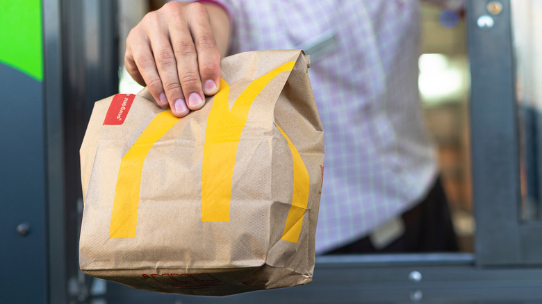 McDonald's employee handing food bag outside drive-thru window