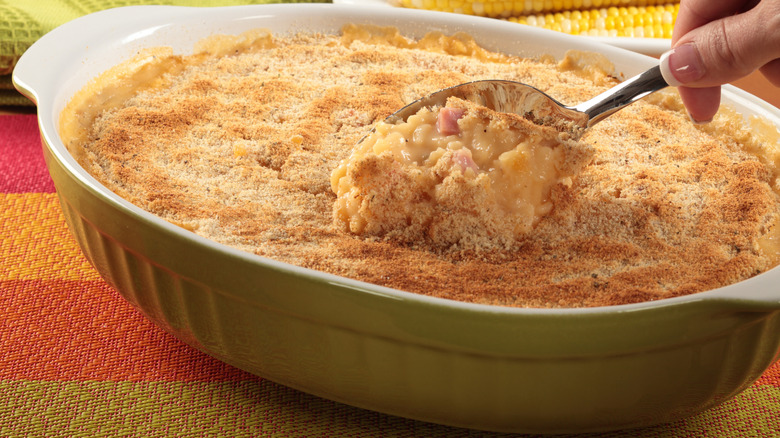 hand sticking spoon in pan of scalloped corn