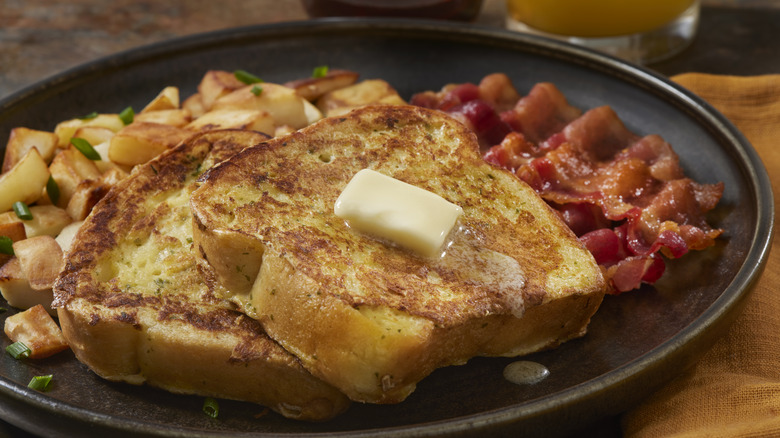 Two slices of French toast served with bacon and home fries