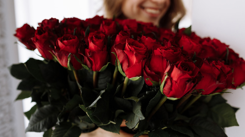 A woman smiles behind a bouquet of red roses