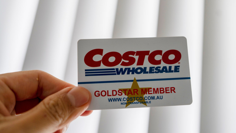 A hand holds a Costco Wholesale membership card against a white background