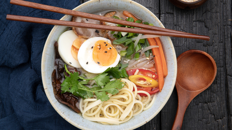 Overhead shot of a bowl of ramen with soft boiled eggs, chopsticks, and a wooden spoon
