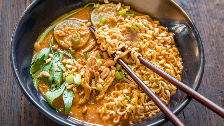 Peanut butter noodles with chopsticks and fresh herbs