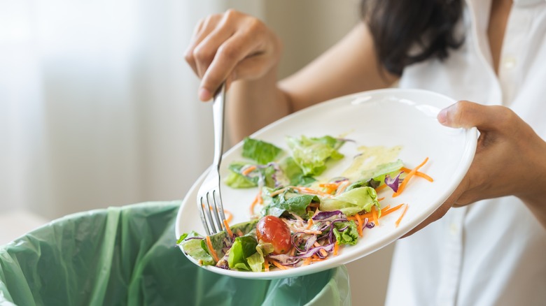 Woman scrapes leftover salad into a compost bin
