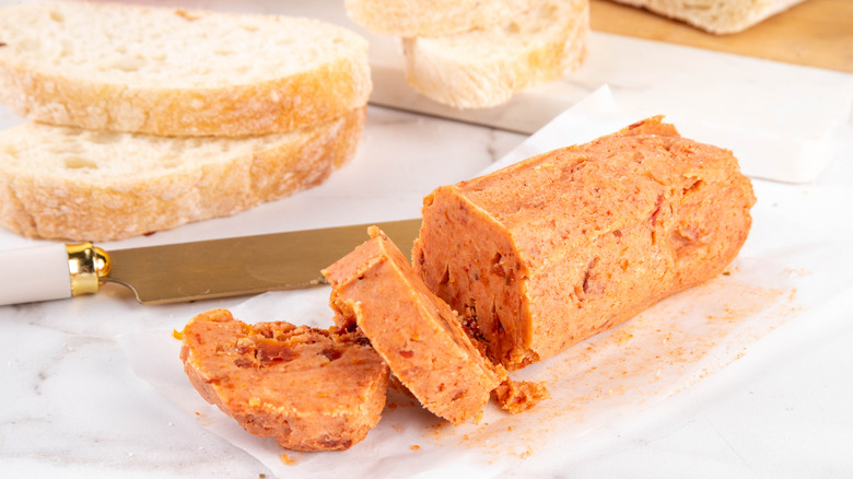 A chunk of clay red compound butter cut into slices sitting near slices of bread.