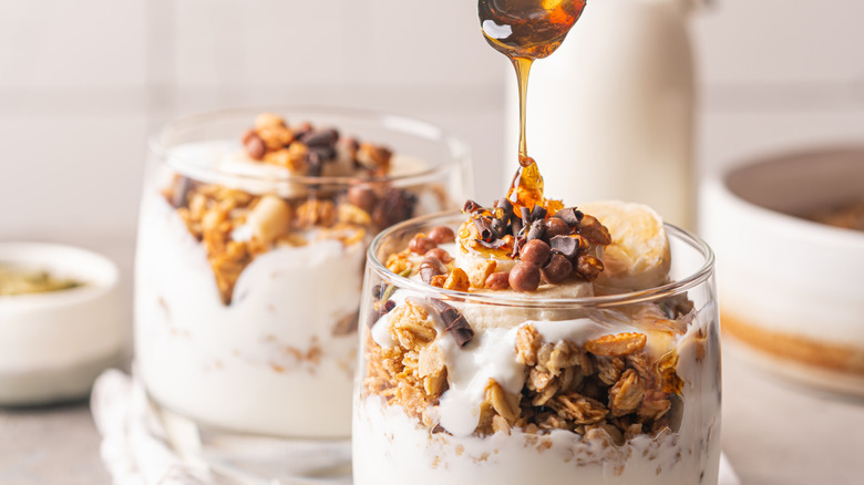 A person spoons honey over a fruit and granola yogurt parfait