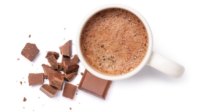 A top-down view of a mug full of hot chocolate with pieces of chocolate beside it.