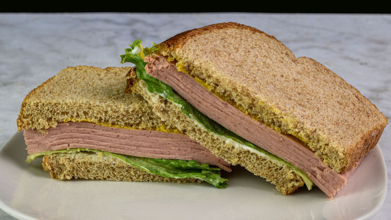 A bologna sandwich with mustard on a white plate on a table