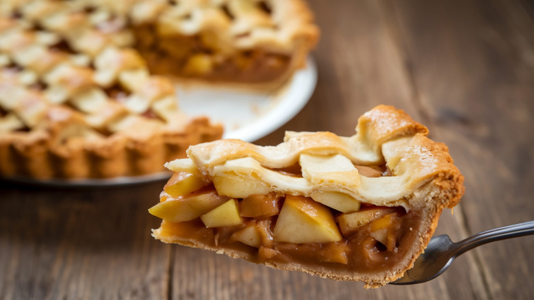 Slice of apple pie with the rest of the pie in the background