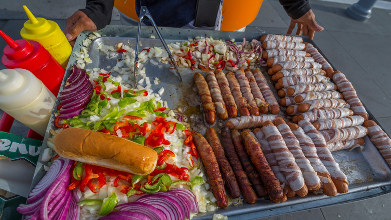 Hot dogs wrapped in bacon, with onions, peppers, and condiments on a street vendor's cart in San Francisco