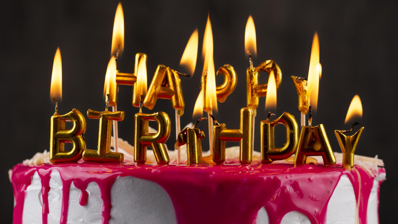 Lit birthday candles melting on top of a cake, with a dark background