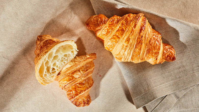 Two croissants on table and linen cloth, with one cut in half