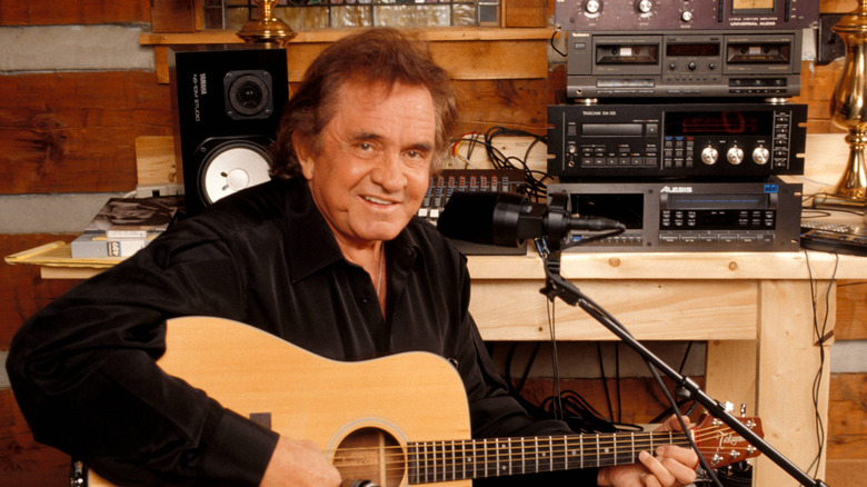 Johnny Cash posing for a portrait with a Takamine acoustic guitar while recording in his home studio.