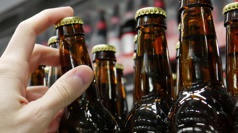 A hand grabbing a bottle of beer from a shelf