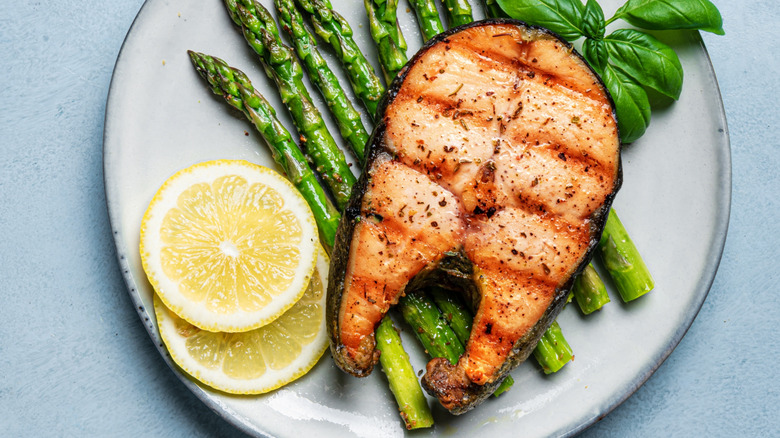 Grilled skin-on bone-in salmon fillet with asparagus, lemon slices, and basil sprig