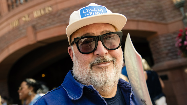 Andrew Zimmern wearing sunglasses and a white hat outside.