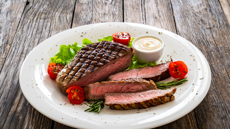 grilled sirloin on a white plate with lettuce, tomatoes, and a cup of white sauce