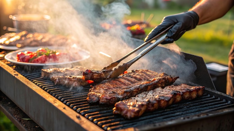 Hand using tongs to adjust ribs on outdoor grill
