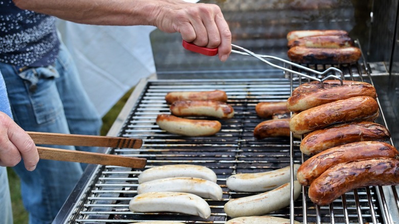 Hands using tongs to adjust sausages on grill