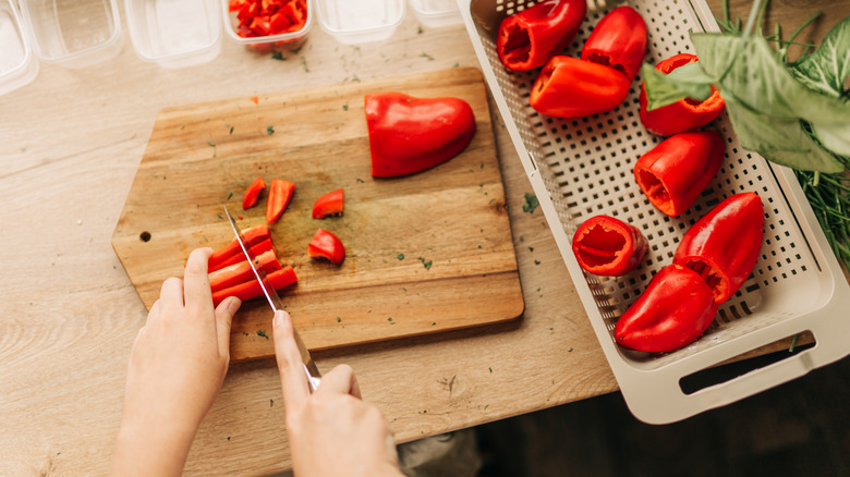 A woman prepping red peppers on a wood cutting board