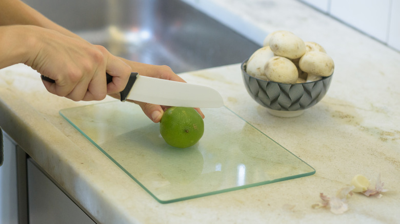 A woman cutting a lime with a knife on a glass cutting board