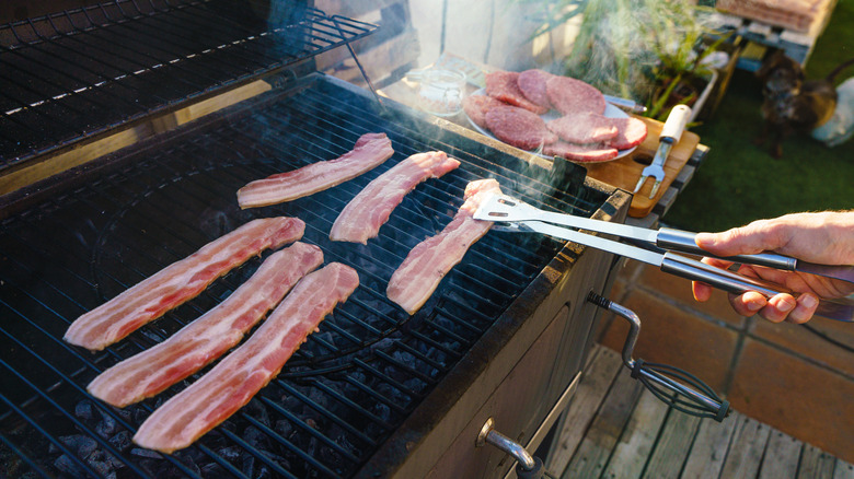 person moving thick-cut grilled bacon with tongs