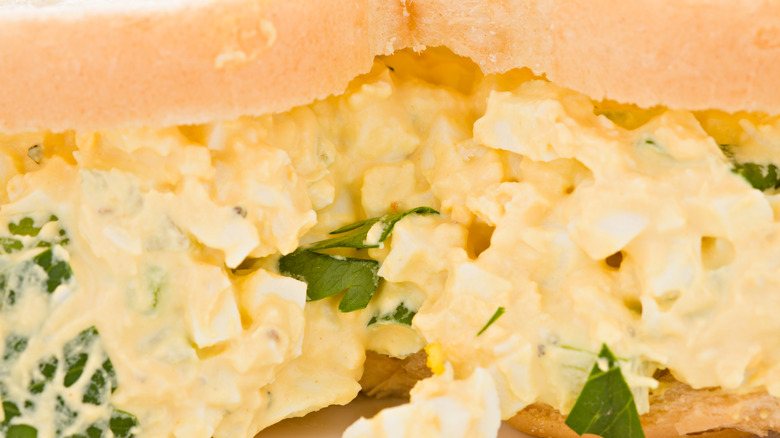 A closeup of a creamy egg salad sandwich with parsley