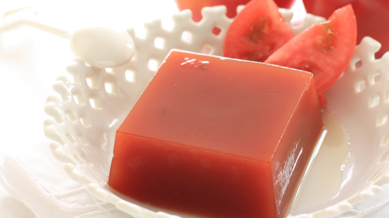 Tomato gelatin in a square shape, served with slices of tomato and a white spoon