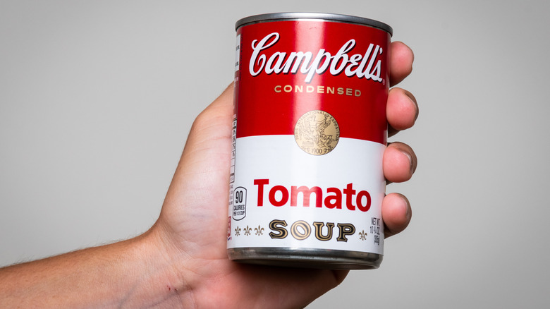 A hand holding a can of classic Campbell's tomato soup