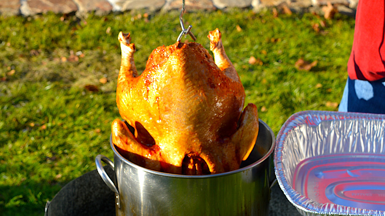 Whole turkey being lifted out of a pan with oil for frying outdoors