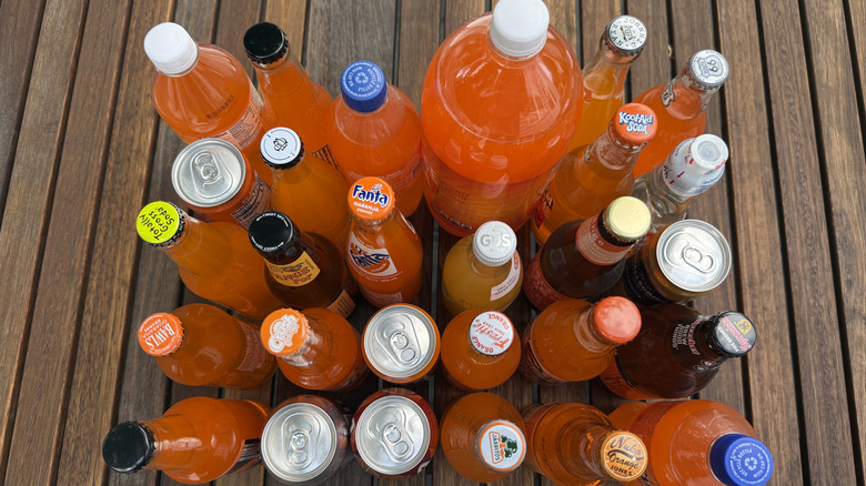 Several bottles and cans of orange sodas