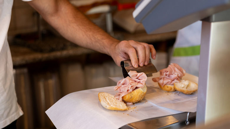 Deli worker placing meat on bread using tongs