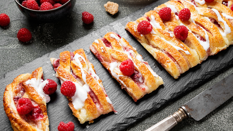 Slices of braided raspberry Danish with fresh raspberries on a slate serving platter