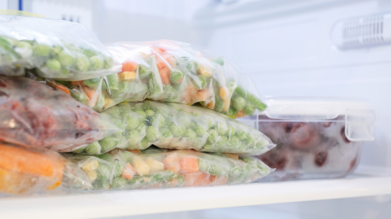 Bags with frozen vegetables and a container with cherries on the shelf in the freezer.