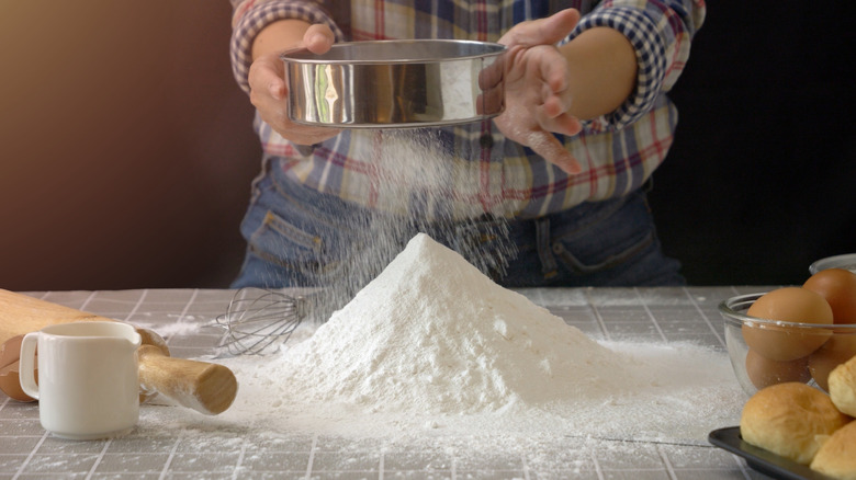 A person uses a sieve to aerate flour for baking
