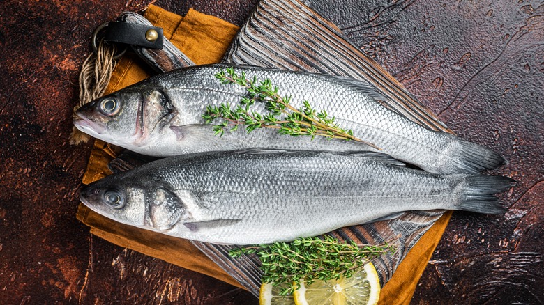 Two raw branzino with rosemary and lemon on a cutting board